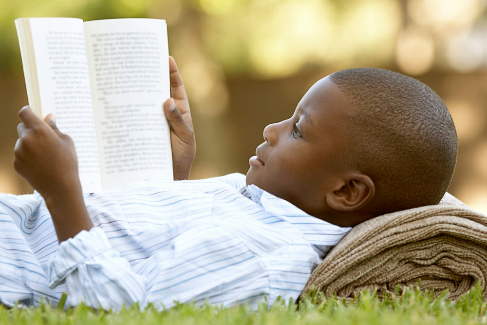 boy reading a book outside in summer