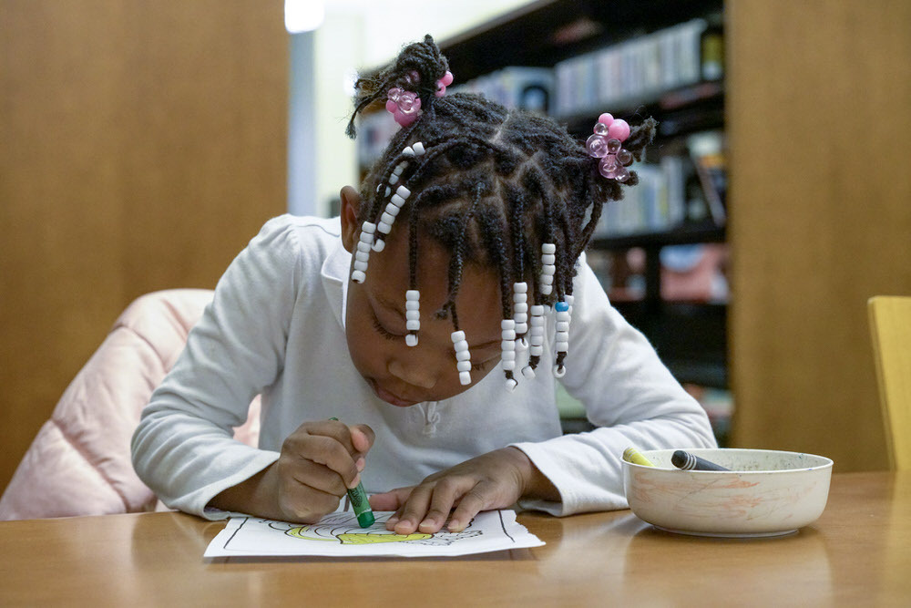 Kids arts and crafts - a girl focused on coloring papers at a library table