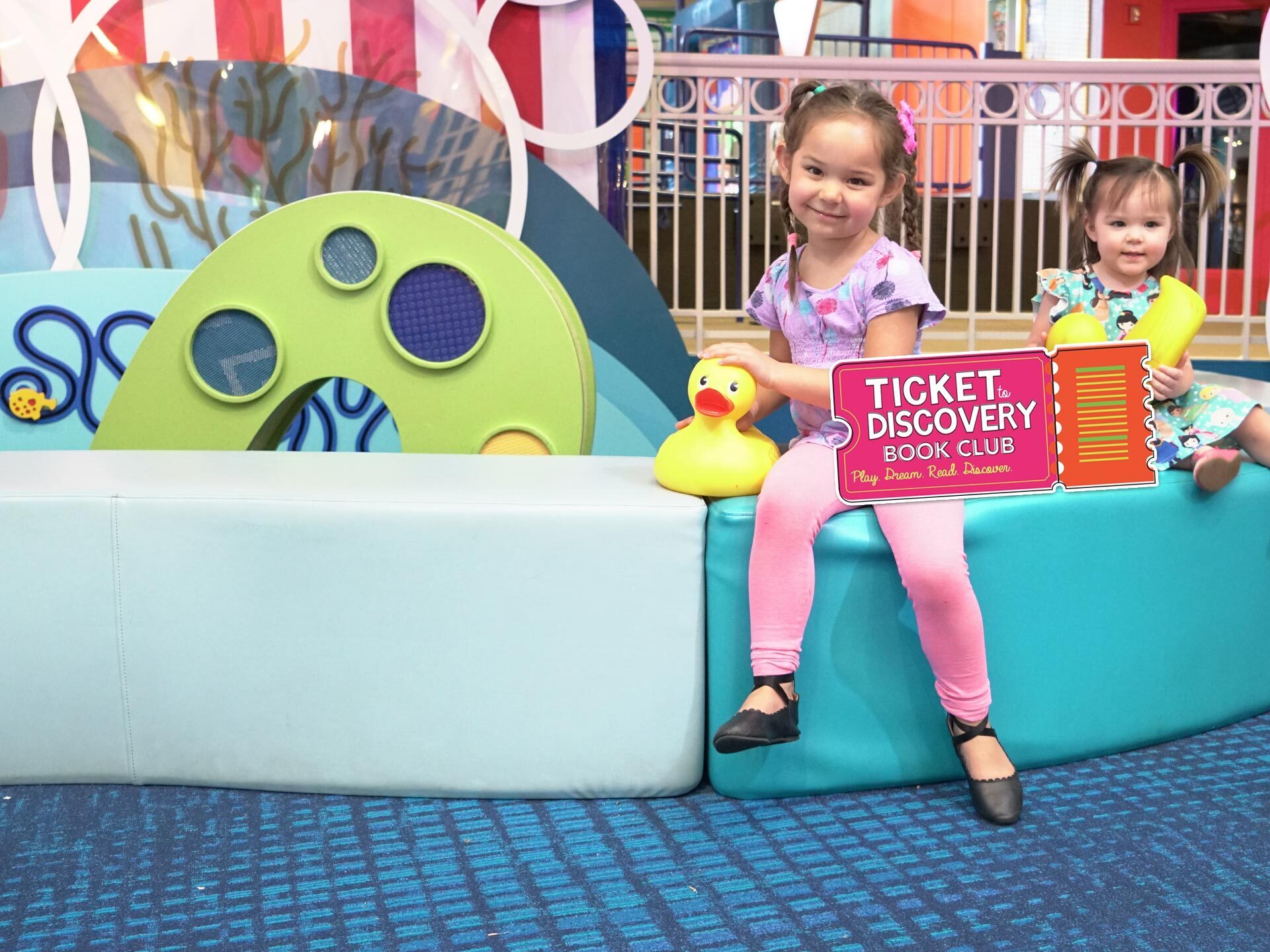 Tickets to Discovery - two young girls with a large colorful ticket in the Port Discovery children's museum
