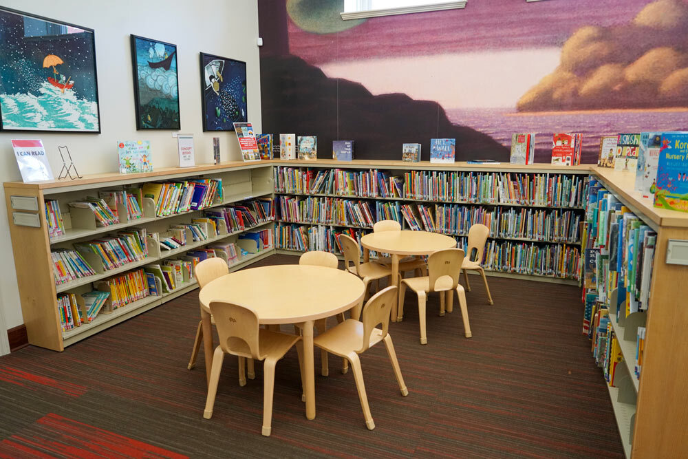 Canton interior view of a children's section with books, tables and chairs, and artwork on the walls