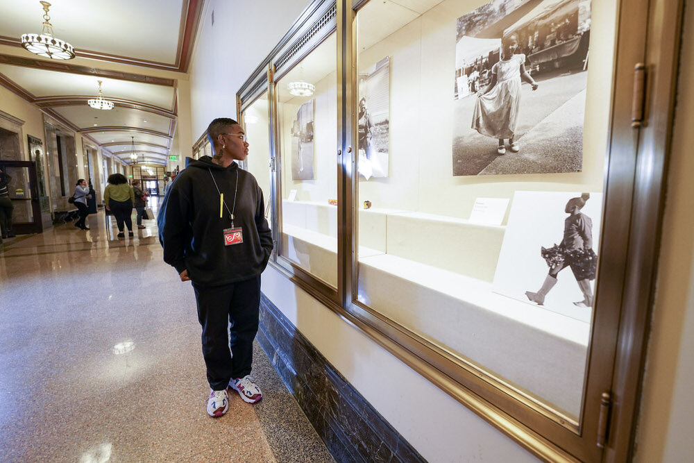 Artist in Residence Shan Wallace by her hallway exhibit, wearing a Pratt ID card