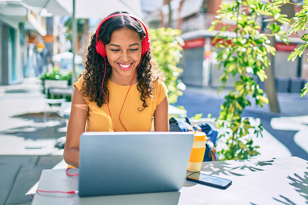 Downloads & Streaming Media - a smiling woman at an outdoor table with a laptop and headphones