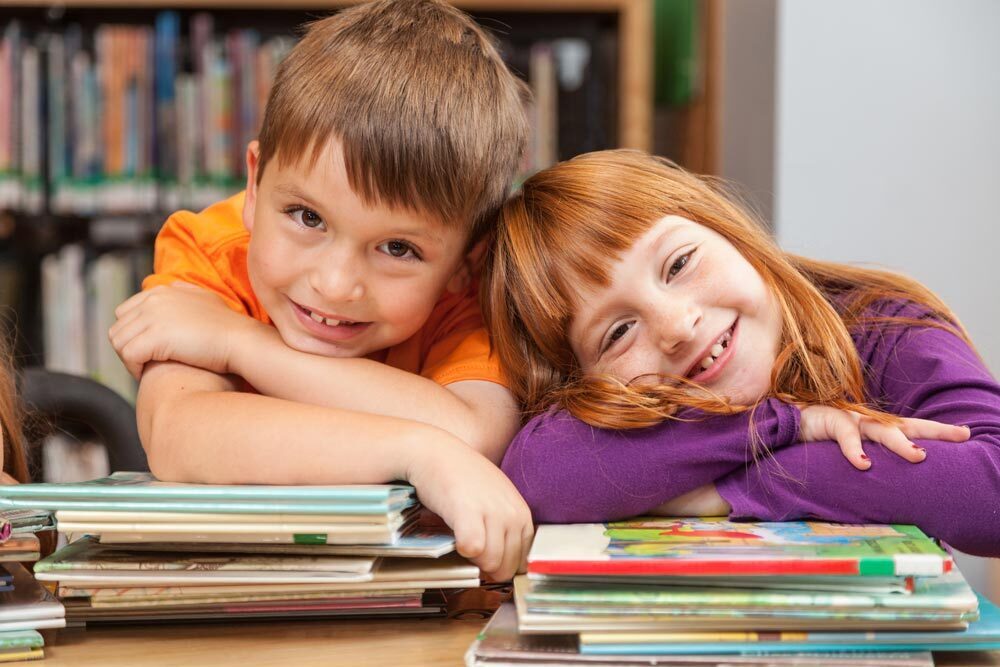 Kids - two smiling children with stacks of children's books