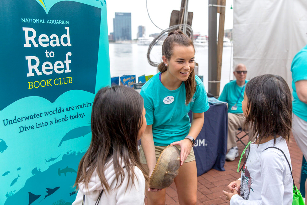 Read to Reef Book Club - youth education helper showing kids a horseshoe crab, promoting Read to Reef