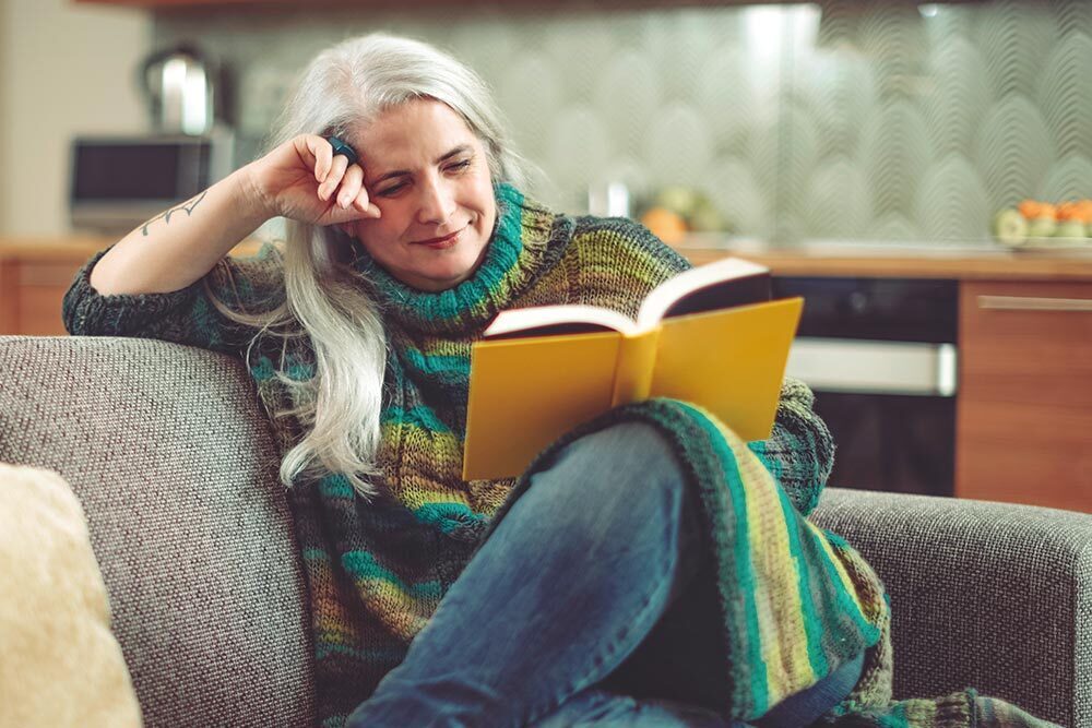 adults - a silver-haired woman reading a book in a cozy home
