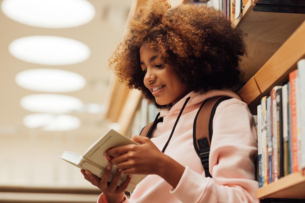 teens - a girl reading a book in the library
