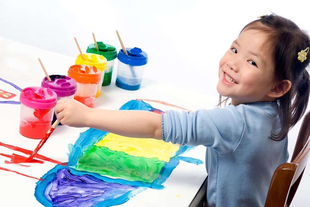 arts and crafts  - young child with art supplies on a table, painting and smiling
