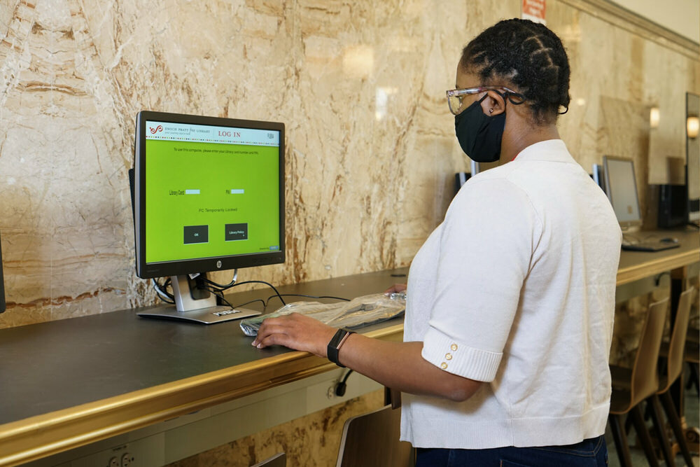 woman using a public library computer with safety precautions in place