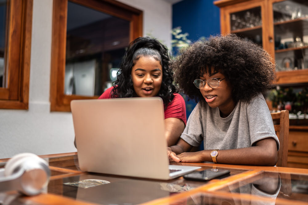 two teens using the internet on a laptop at home