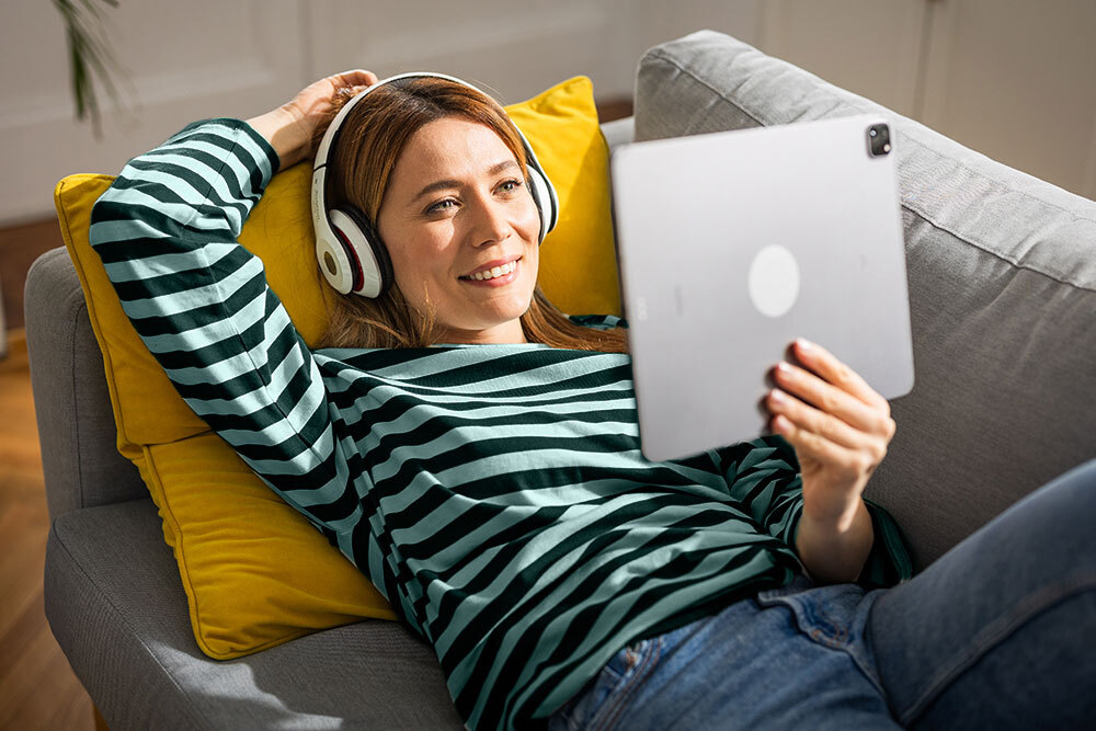Downloads & Streaming Media - a smiling woman at home on a couch table with a digital tablet and headphones