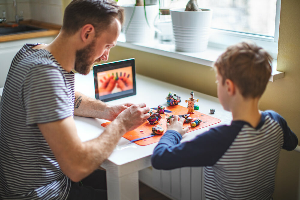 homeschooling dad and son doing arts crafts with clay and a digital tablet 3x2
