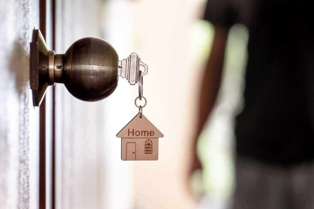 house key and keychain in a doorknob with a person in the background - housing navigators
