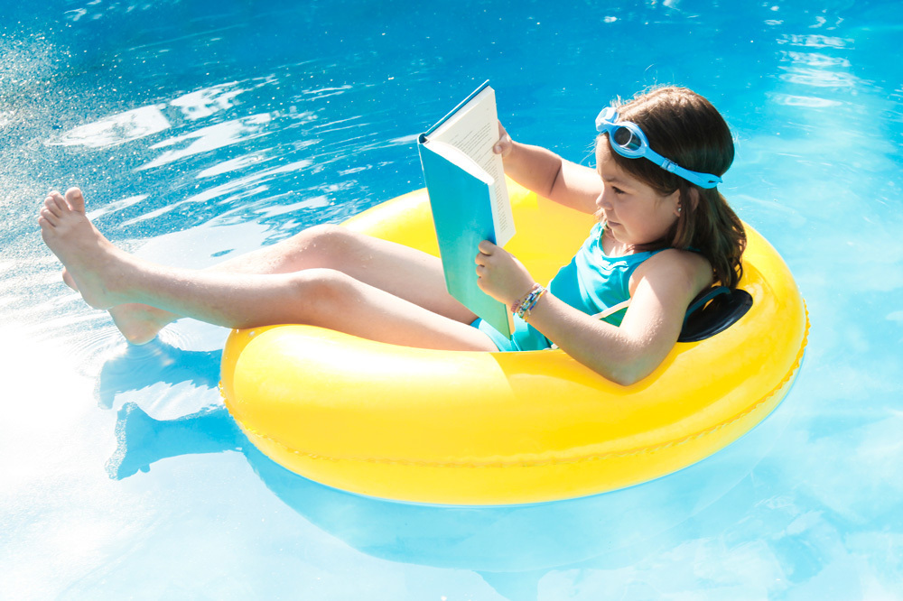 child in a pool floatie reading a book