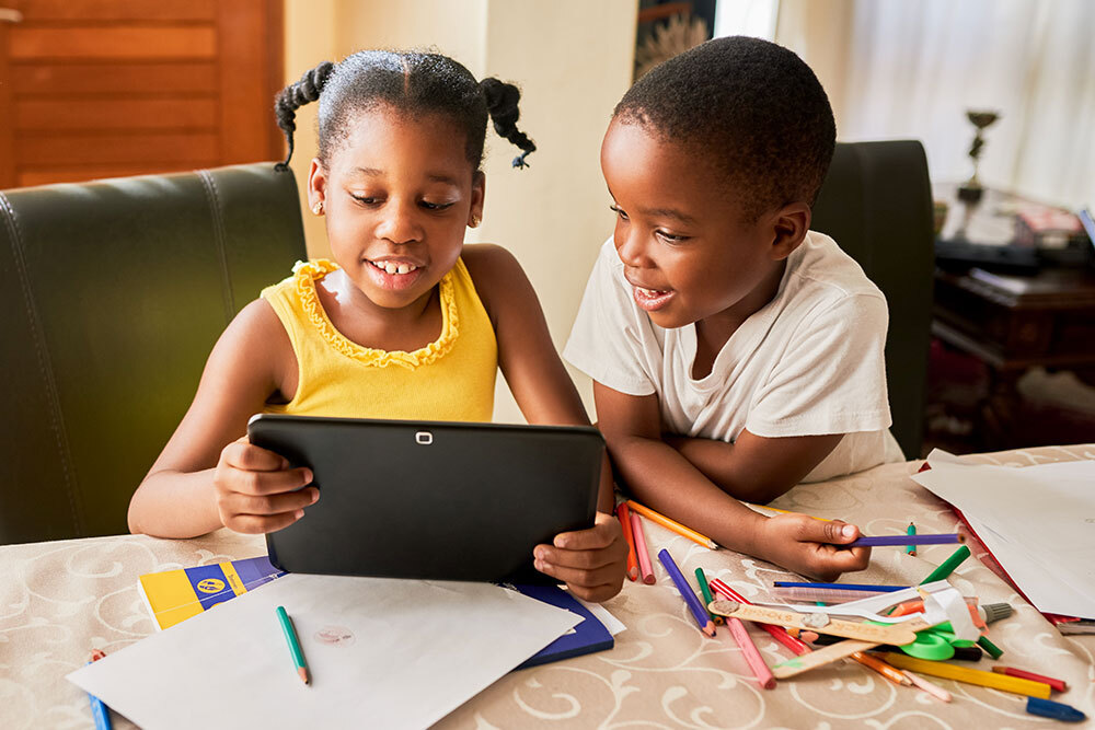 two kids at home with a digital tablet and coloring supplies