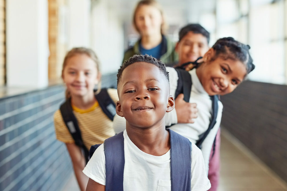 kids ina  school hallway with backpacks, boy in front