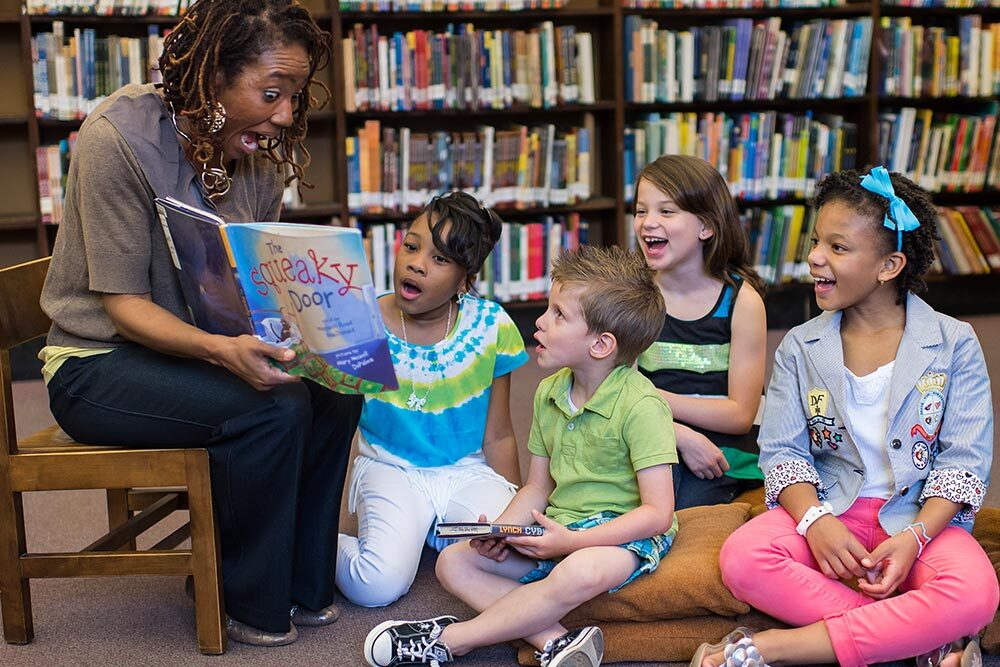 storytime events for kids - Pratt librarian reading a book and group on the floor.