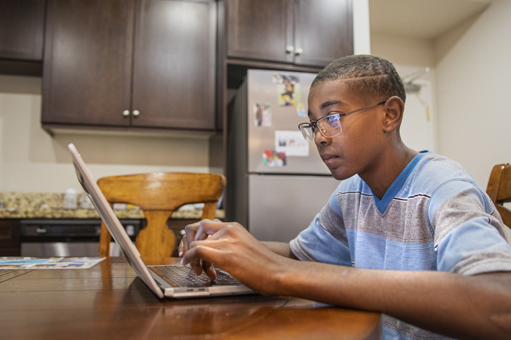 boy studying in home kitchen with a laptop