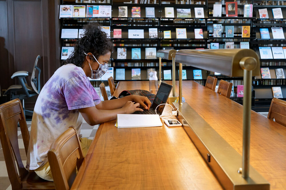 doing online research at a Central Library table with a laptop, phone, and notebook