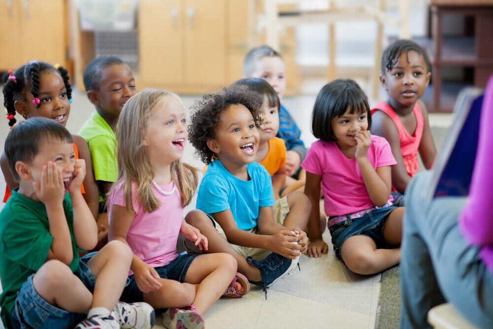 storytime - group of expressive young children on the floor listening to a story.