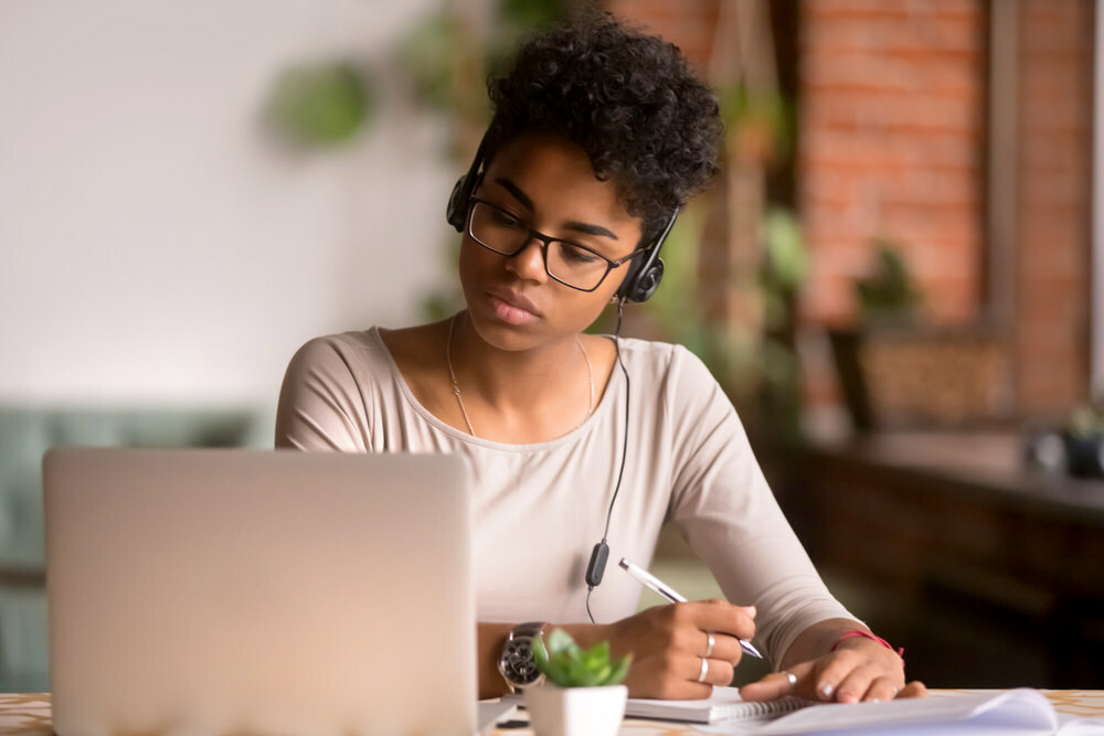 serious young woman using laptop with headphones, taking notes