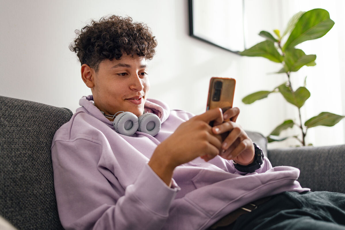 teenage boy wearing headphones, using a phone.