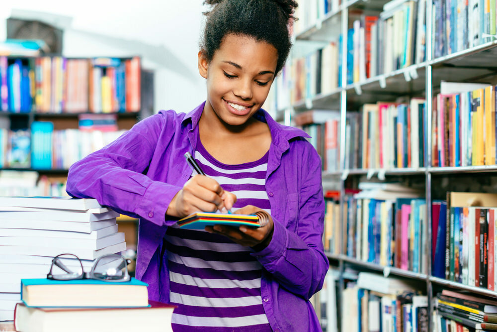 teen girl surrounded by books, writing in a notepad