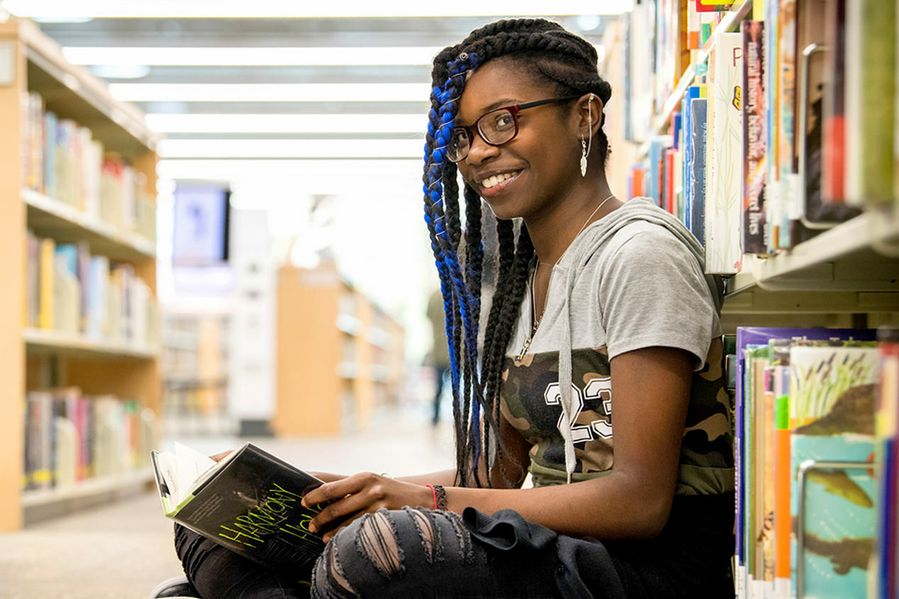 teen girl smiling, sitting on the floor with a book at the library