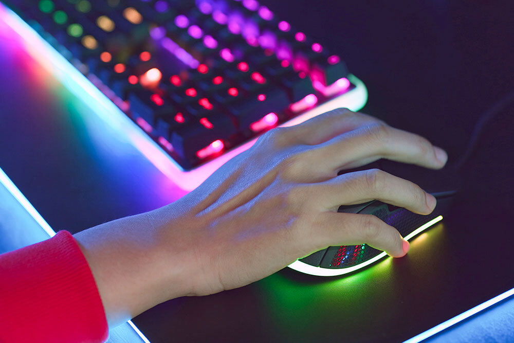 Teens gaming - hand on a computer mouse with rainbow lit keyboard