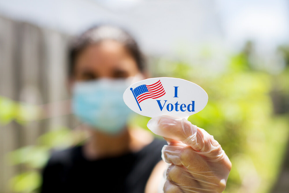 Voting - woman holding an I Voted sticker with COVID mask and gloves