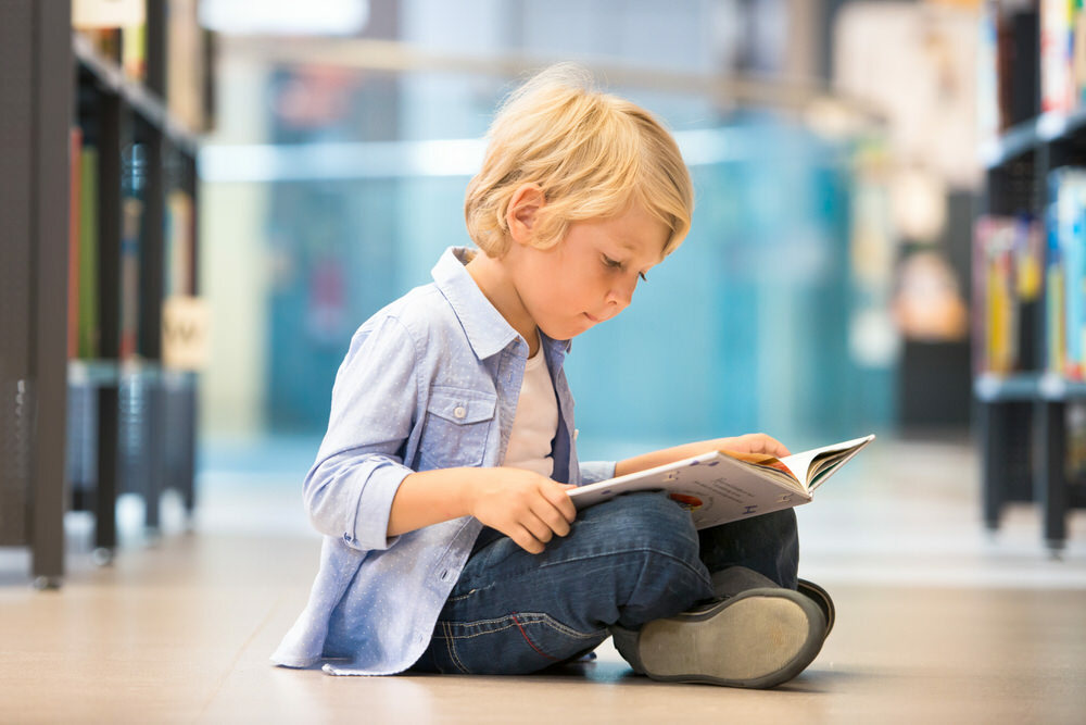 young boy with book on the library floor