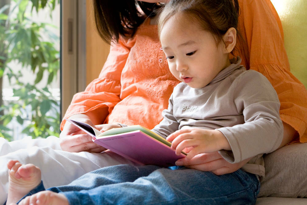 mom and young daughter reading by the window