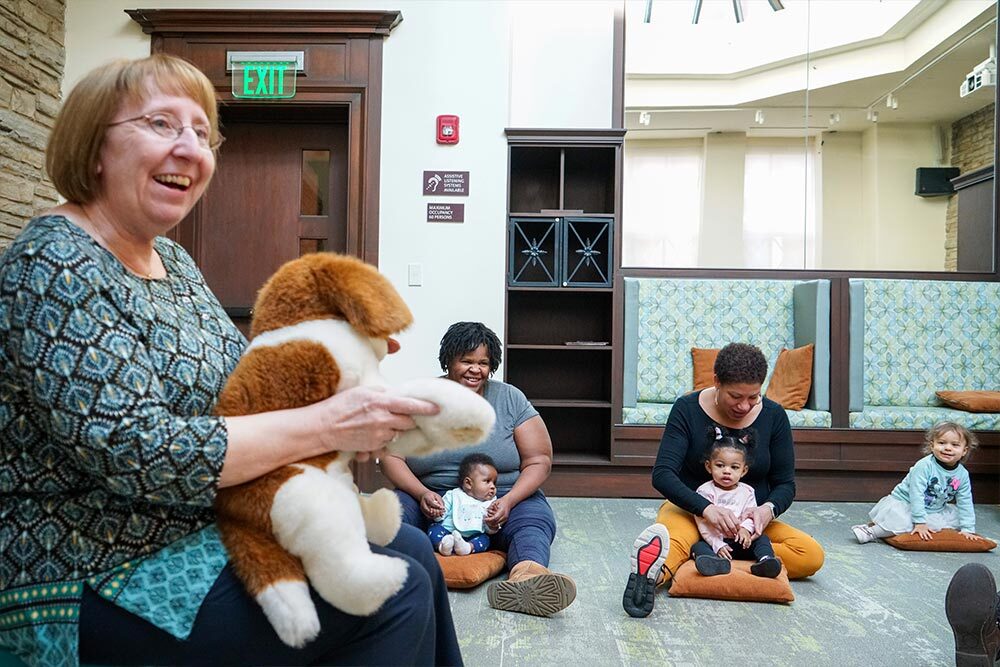 Young children storytime - cheerful librarian with a stuffed animal, and  toddlers and parents on the floor