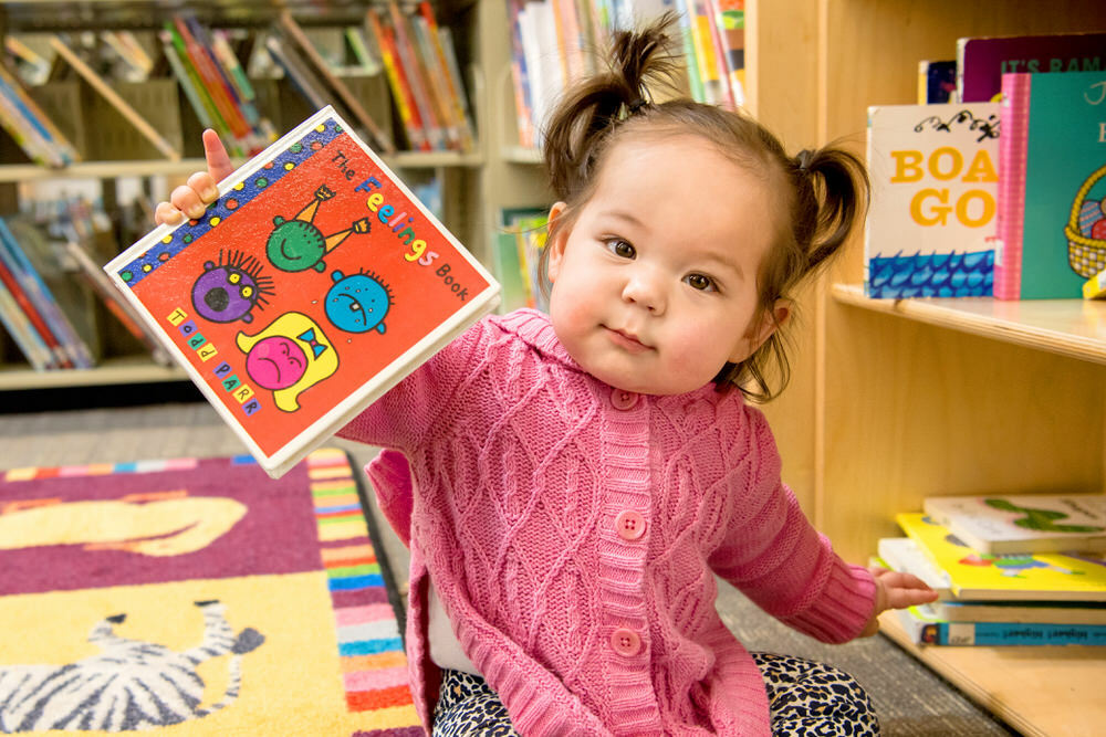 young child on the floor of the library holding a book