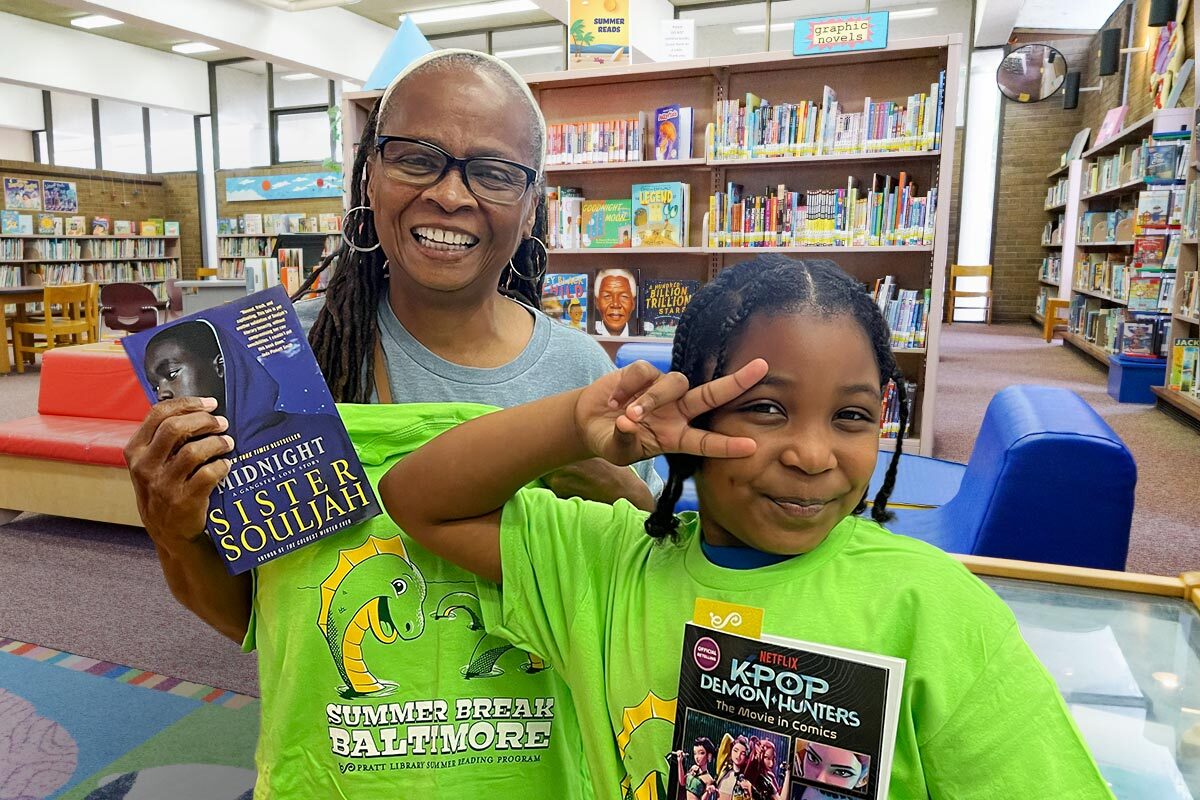 smiling people wearing their 2026 Summer Break Baltimore shirts in the library with their free books.