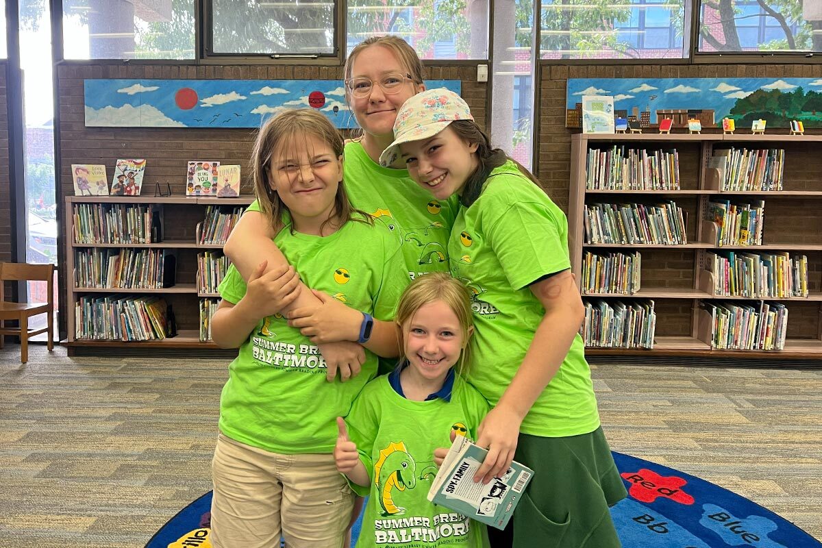 a family wearing their Summer Break Baltimore t-shirts at their branch library.