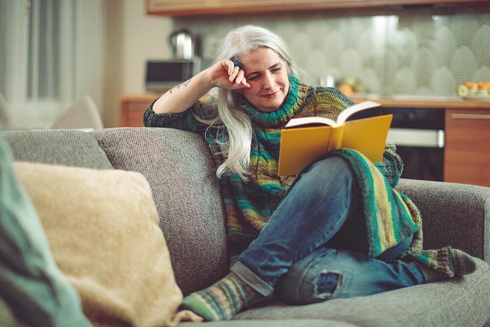 adults - silver-haired woman reading a book in a cozy home