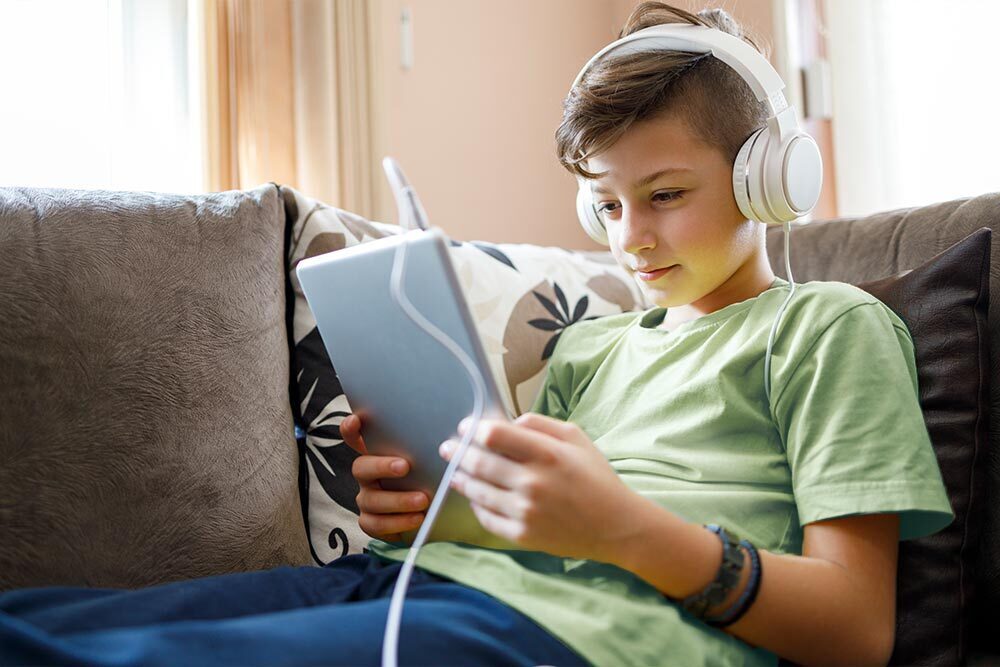kids - a boy with a tablet wearing headphones on a couch