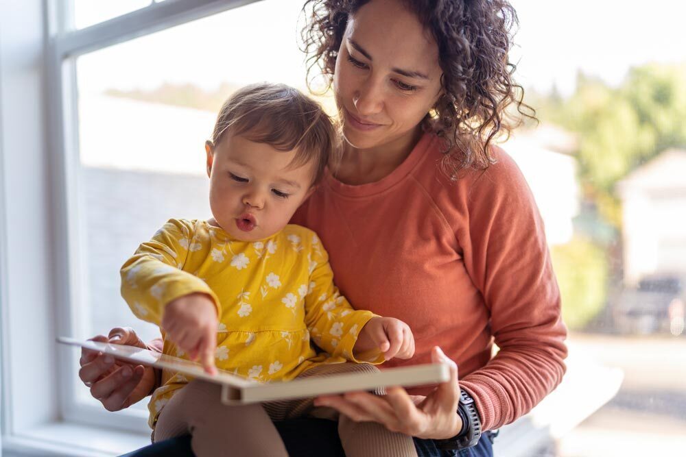 baby and mother reading a book by the window.