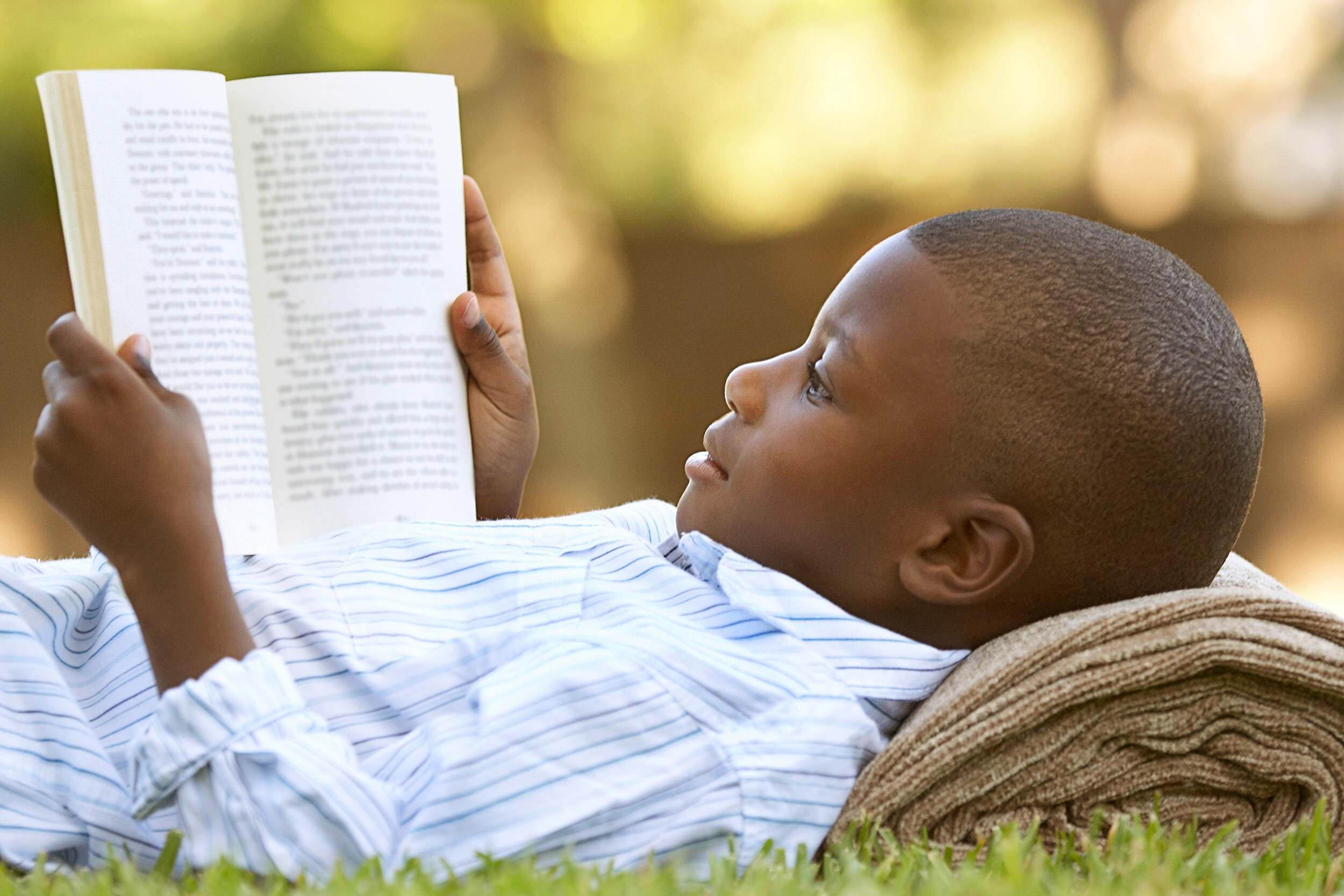kids age group - boy reading a book outside in summer