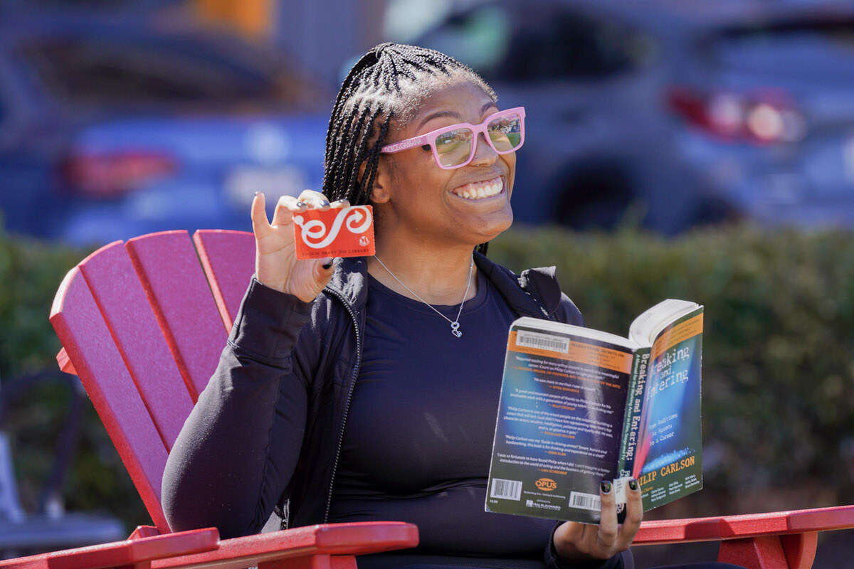 woman outside smiling with a book and Pratt Library card.