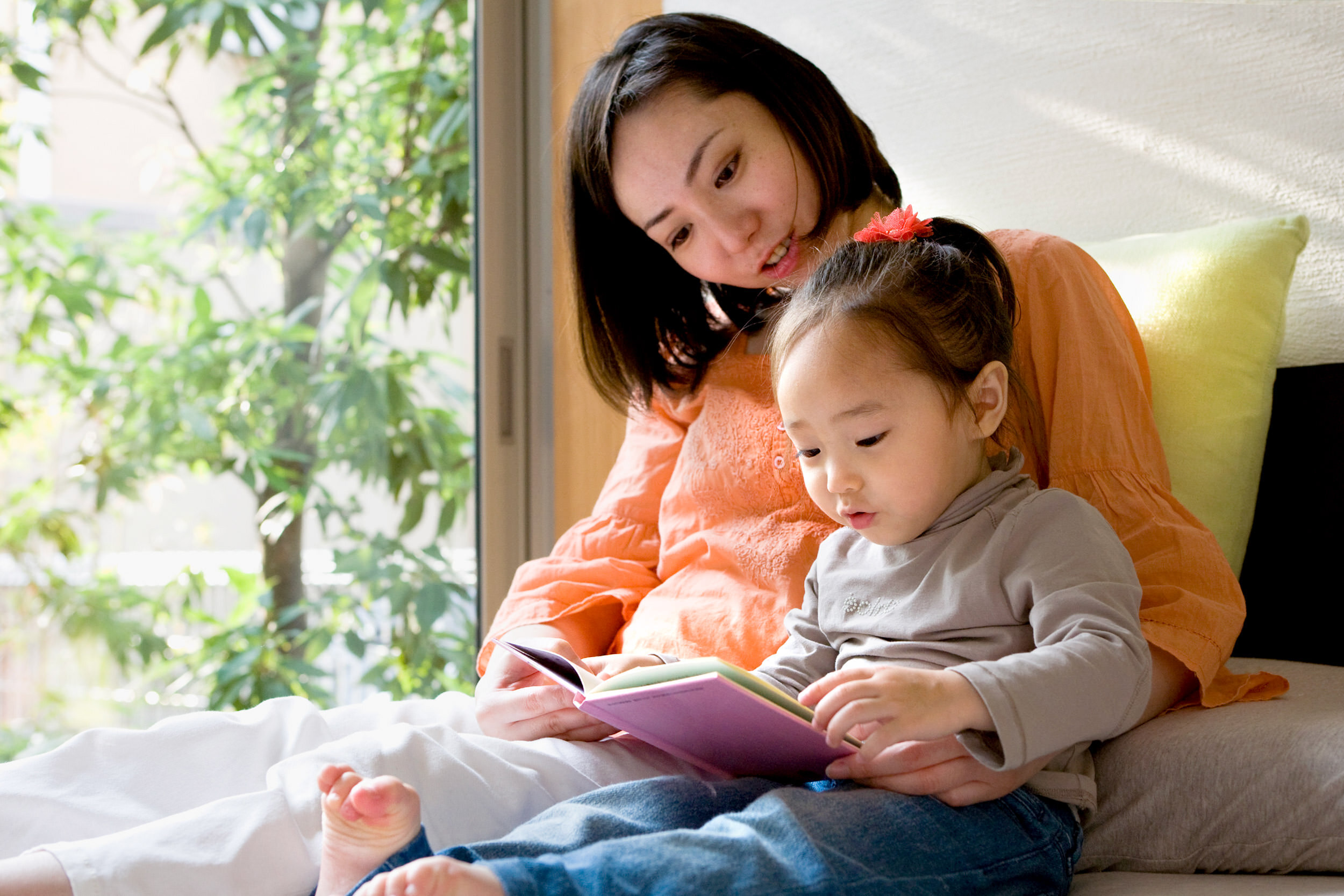 young children - mom and young daughter reading a book by the window