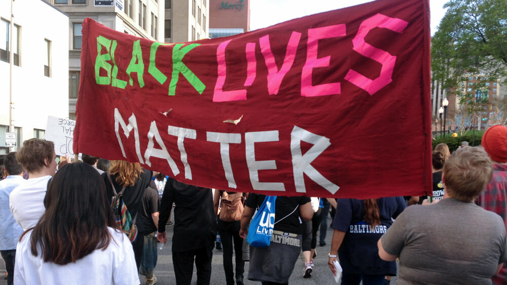 people in Baltimore marching and holding a protest sign reading Black LIves Matter, from surgebaltimore.org