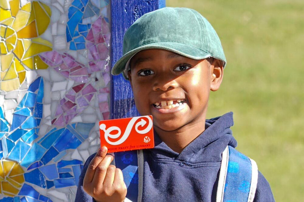 boy holding a Pratt Library card by the Johnston Square Branch mosaic sign