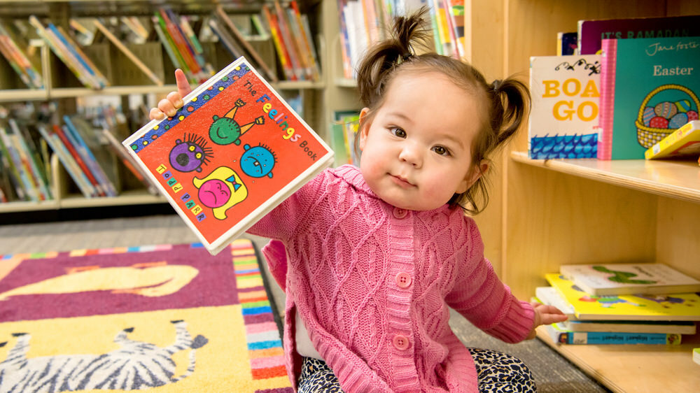 young child on floor of library with a book