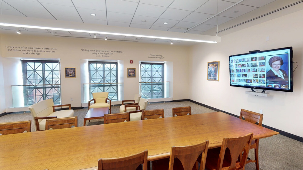 Mikulski Room - walnut table and chairs, digital screen, and windows with quotes above