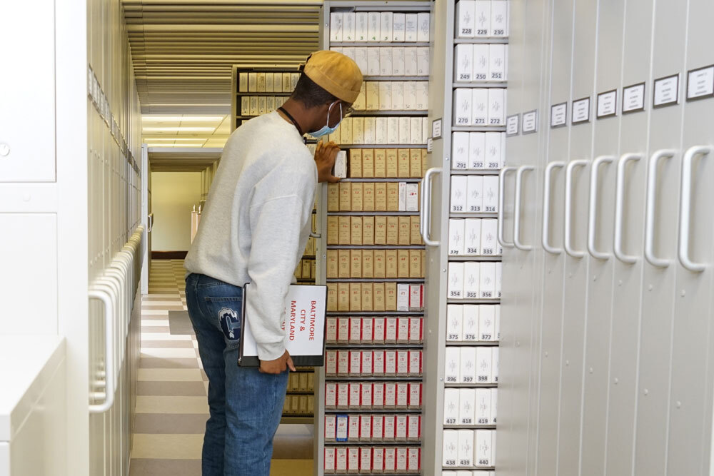 man wearing a mask, looking at boxed microfilm reels in the Periodicals Department