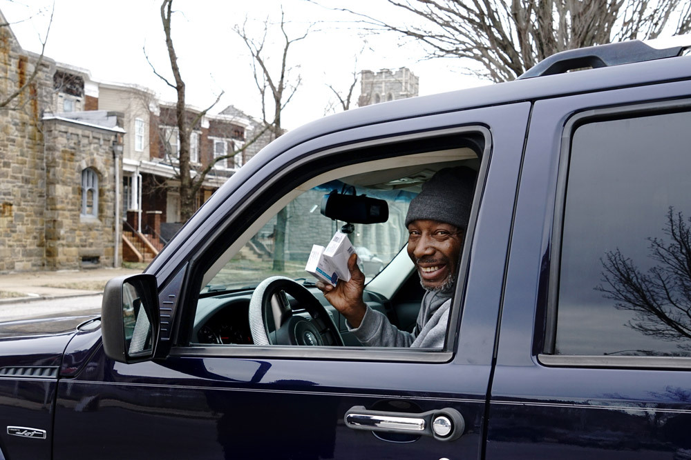 a smiling customer with free at-home COVID-19 test kits in their car