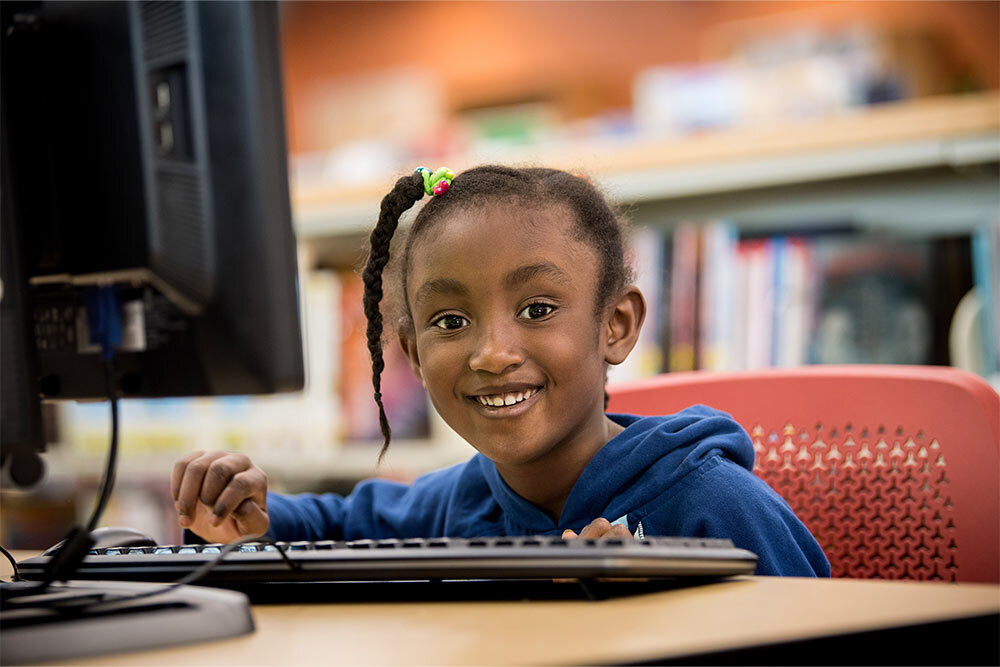 public computers - girl smiling at keyboard in the library