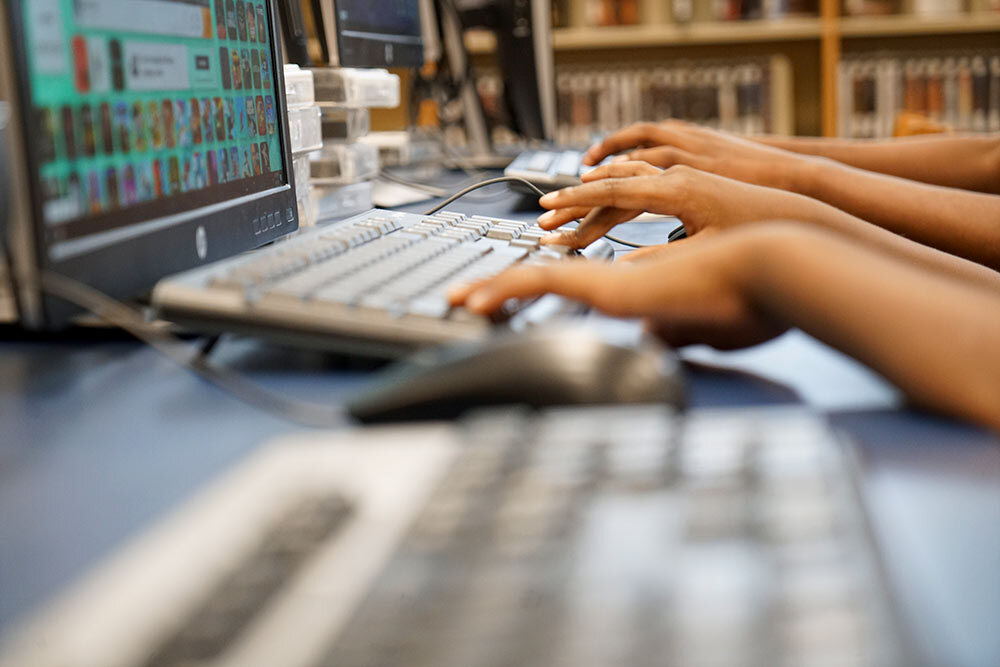 public computers - multiple hands in a row typing on keyboards in the library