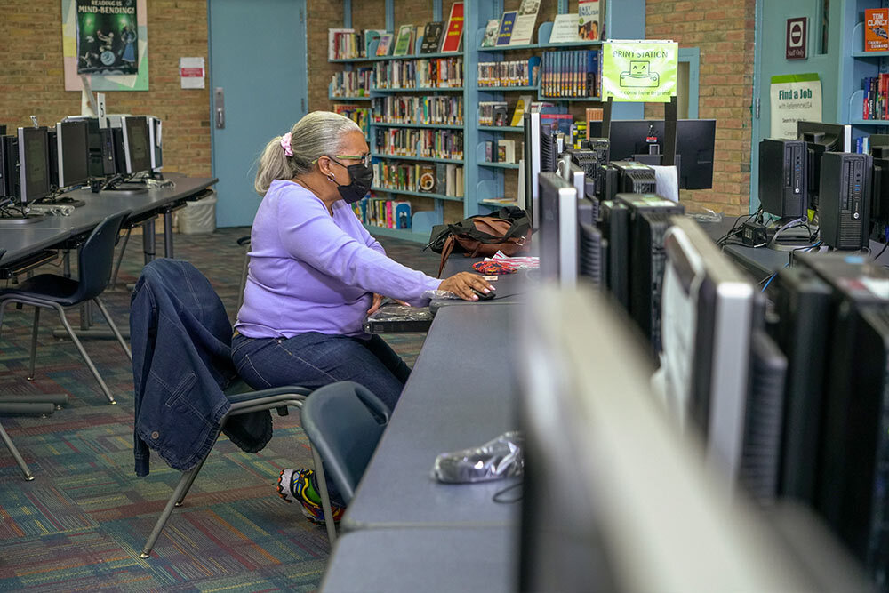 public computers - woman mask using a computer at a library branch with a print station sign in the background